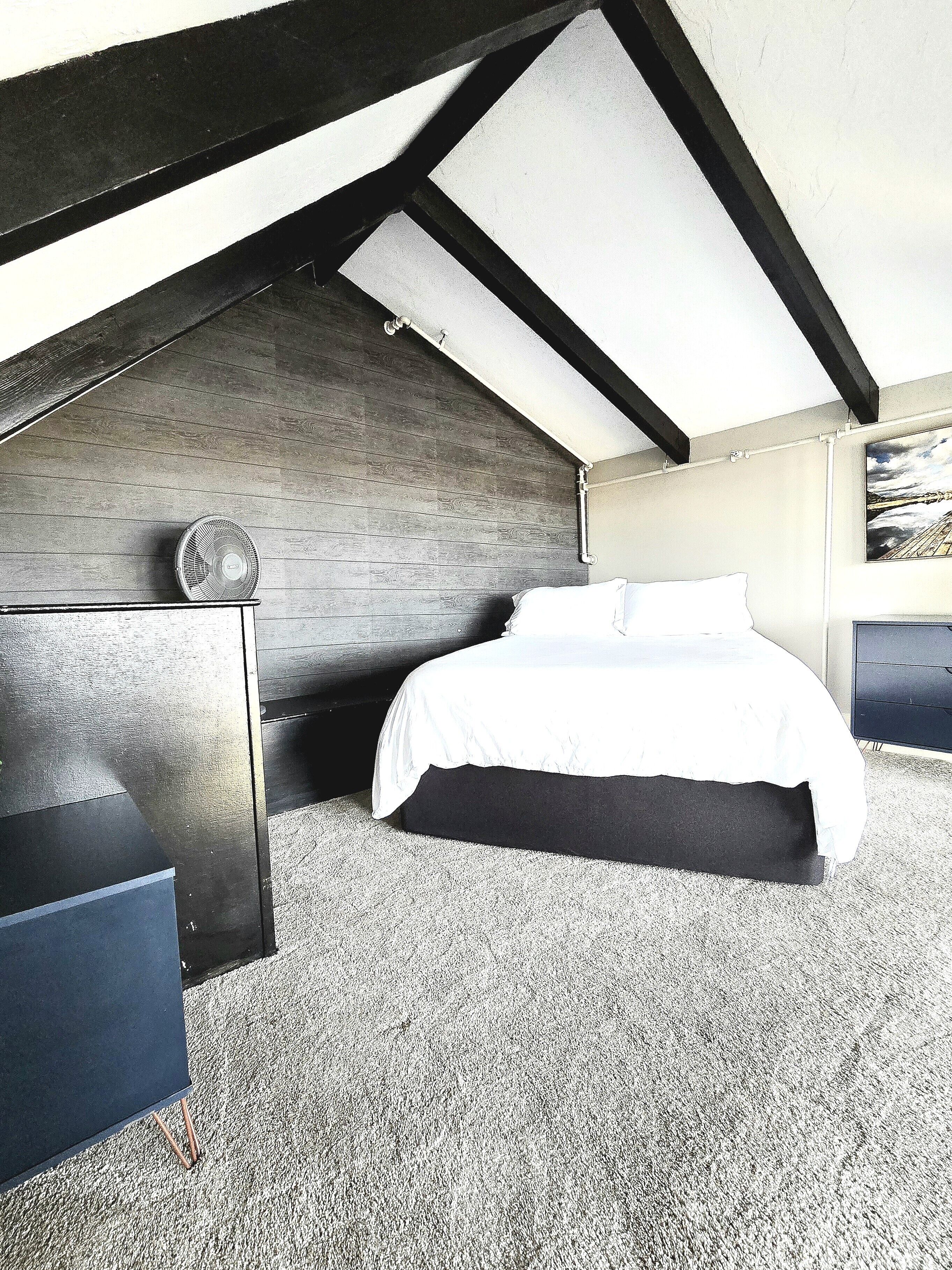 Une chambre avec un plafond en pente, un lit, une commode et un ventilateur.