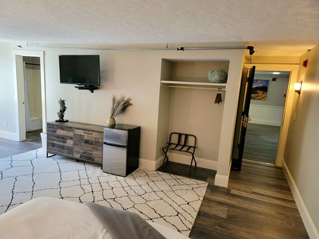 A modern bedroom with a bed, a dresser, a TV, and a walk-in closet.