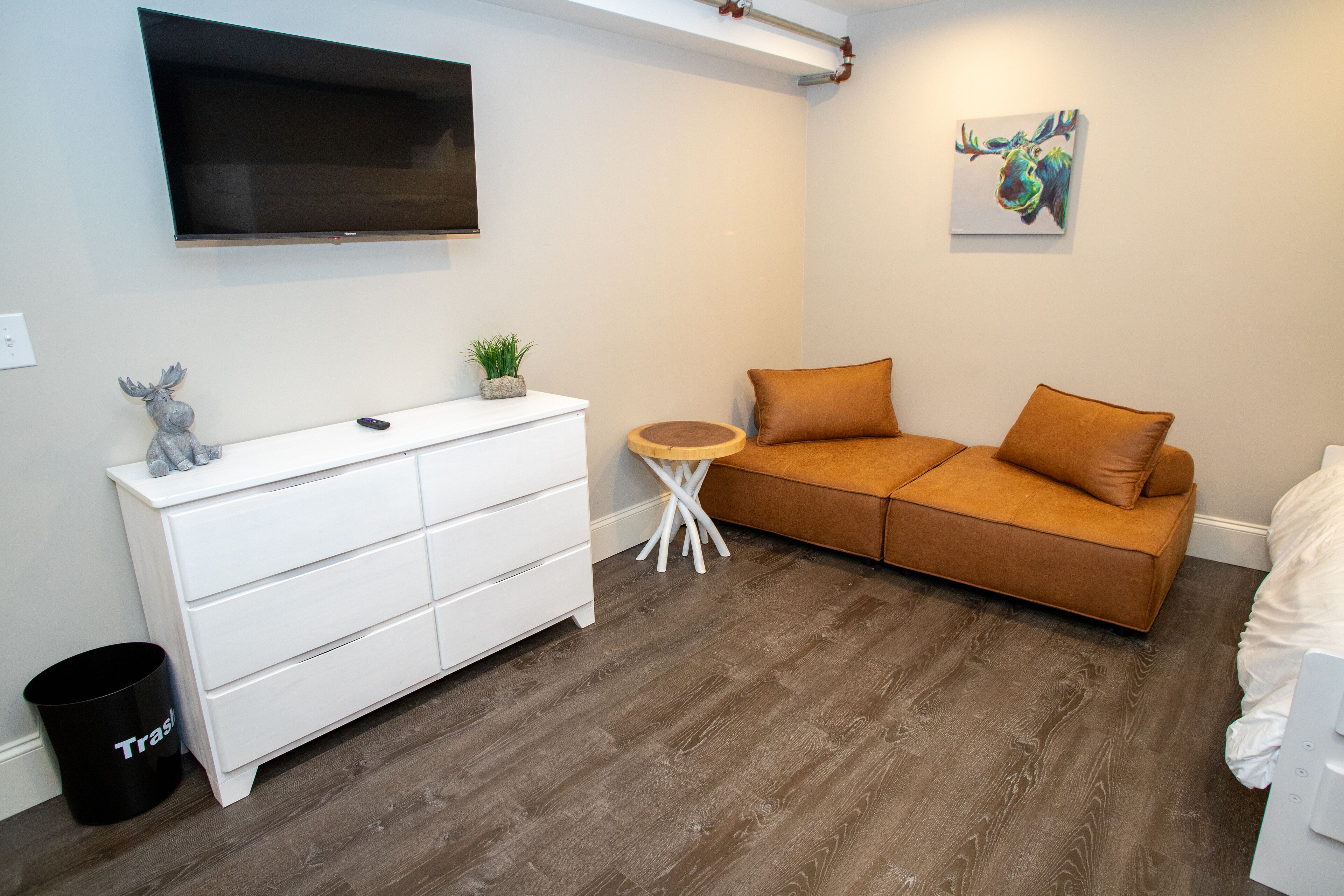 A modern bedroom with a white dresser, a brown sofa, a small round table, and a mounted TV.