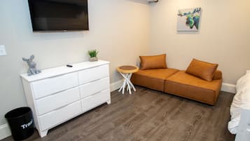 A modern bedroom with a white dresser, a brown sofa, a small round table, and a mounted TV.
