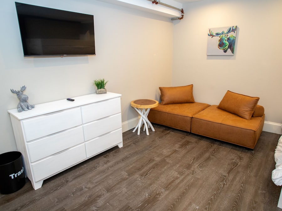A modern bedroom with a white dresser, a brown sofa, a small round table, and a mounted TV.