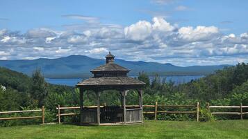 A gazebo in a grassy field with a lake and mountains in the background.