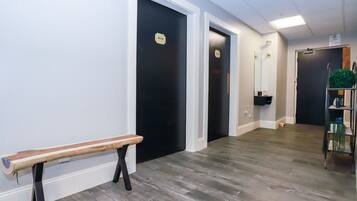 Un couloir avec un banc, des portes noires, un miroir et une étagère sur laquelle sont posés divers objets.