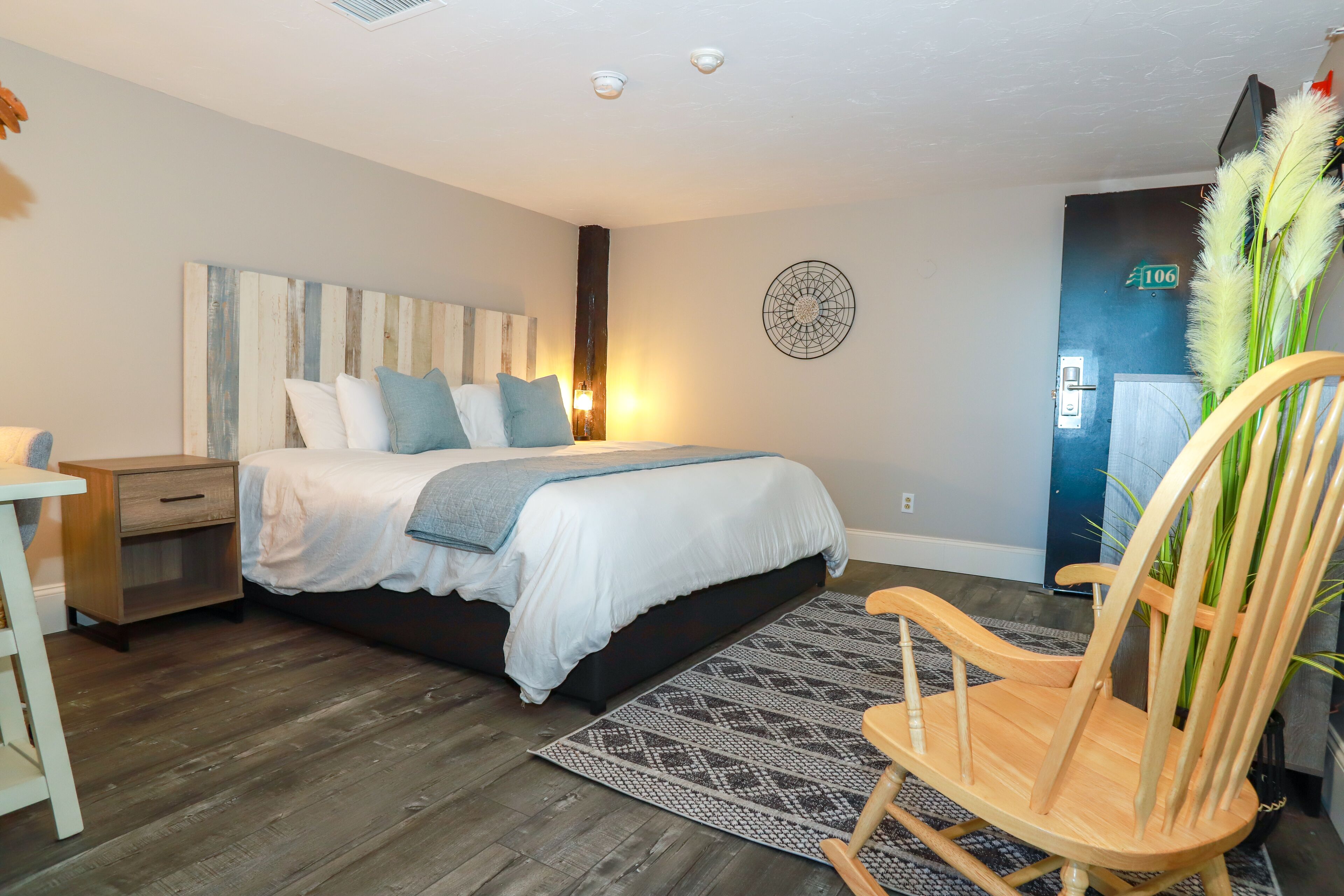 Un dormitorio con cama, mesita de noche, silla y un cuadro decorativo en la pared.