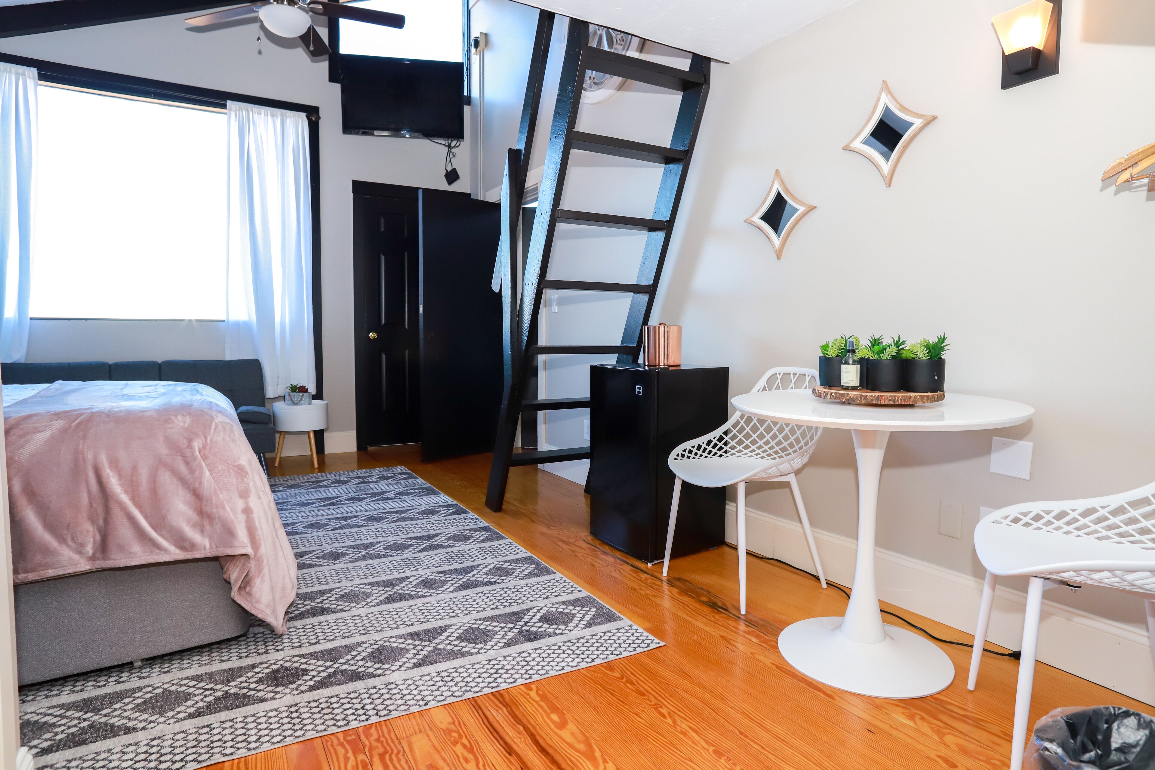 A modern bedroom with a bed, a ladder, a desk with chairs, and a small table with plants.