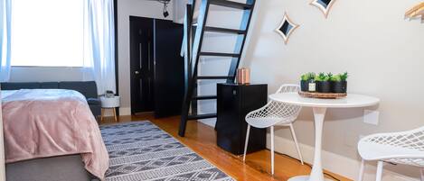 A modern bedroom with a bed, a ladder, a desk with chairs, and a small table with plants.