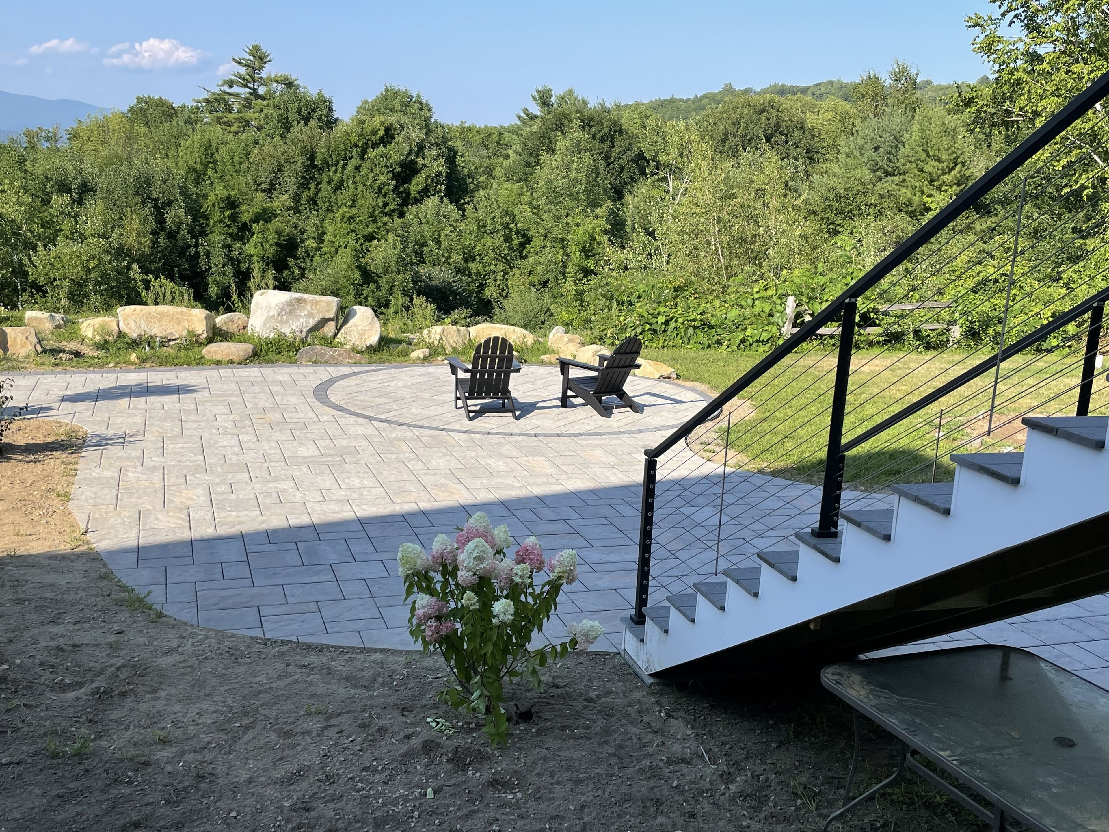 A patio with a stone floor, two Adirondack chairs, and a small flower arrangement.
