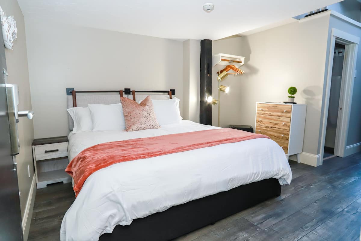 A modern bedroom with a large bed, a nightstand, a dresser, and a wall-mounted light fixture.