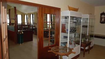 A dining area with a wooden door, a round table with a ship's wheel, and a glass display cabinet with various items.