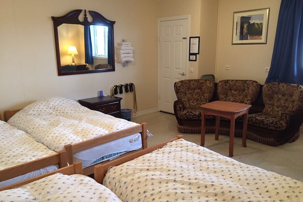 A hotel room with two beds, a chair, a small table, a mirror, a door, and a framed picture on the wall.