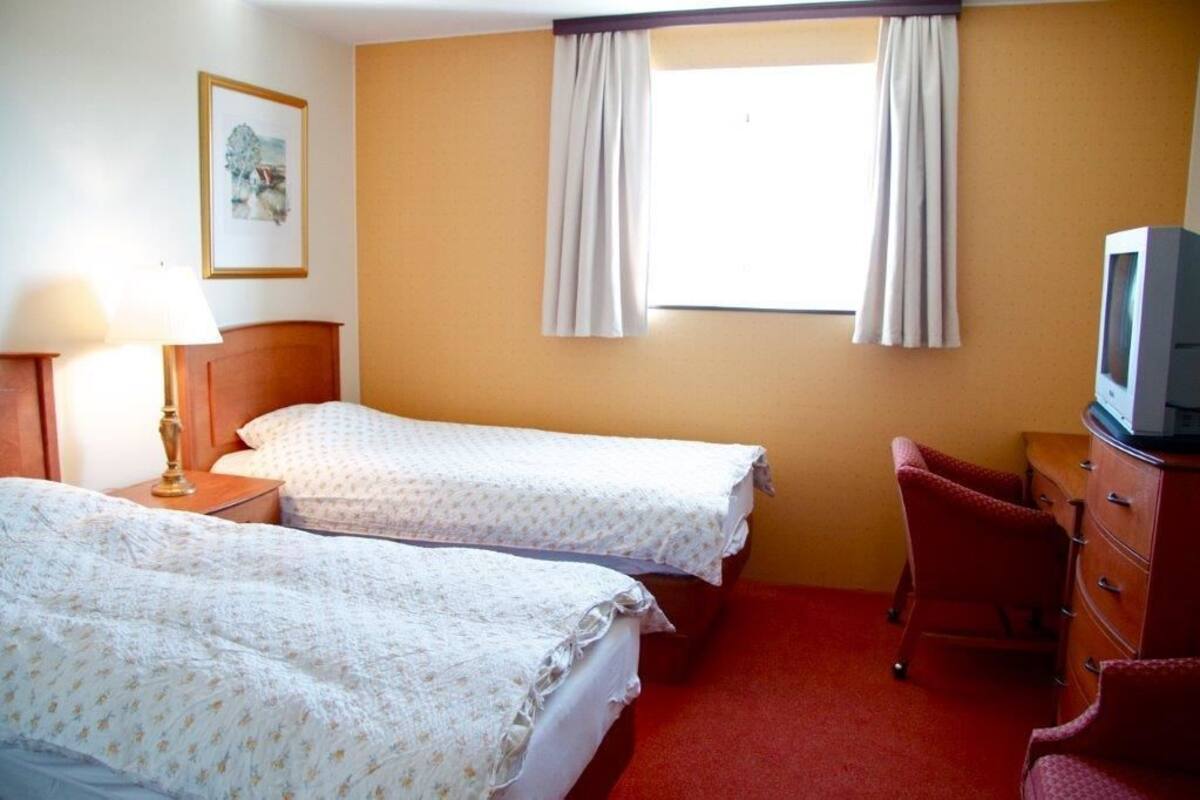 A hotel room with two beds, a TV, a dresser, and a window with curtains.