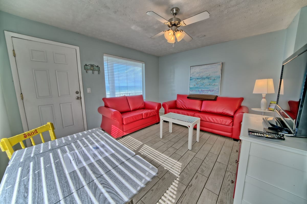 A living room with a red sofa set, a white coffee table, a ceiling fan, and a painting on the wall.
