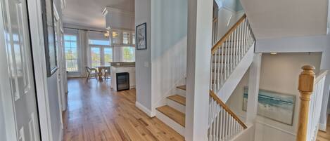A spacious hallway with hardwood floors, a staircase with white railings, and a dining area with a table and chairs.