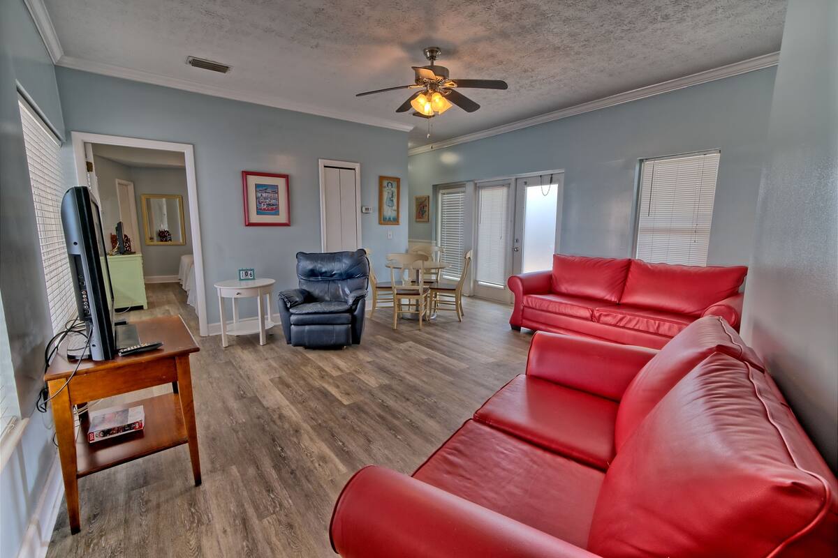 A living room with a red leather sofa, a black leather chair, a wooden coffee table, and a ceiling fan.