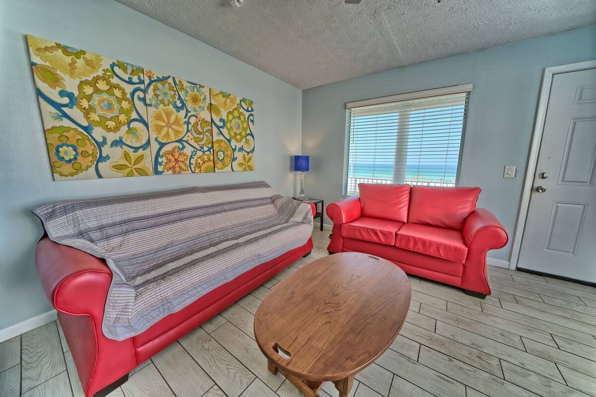 A living room with a red sofa, a striped couch, a wooden coffee table, and a large floral painting on the wall.
