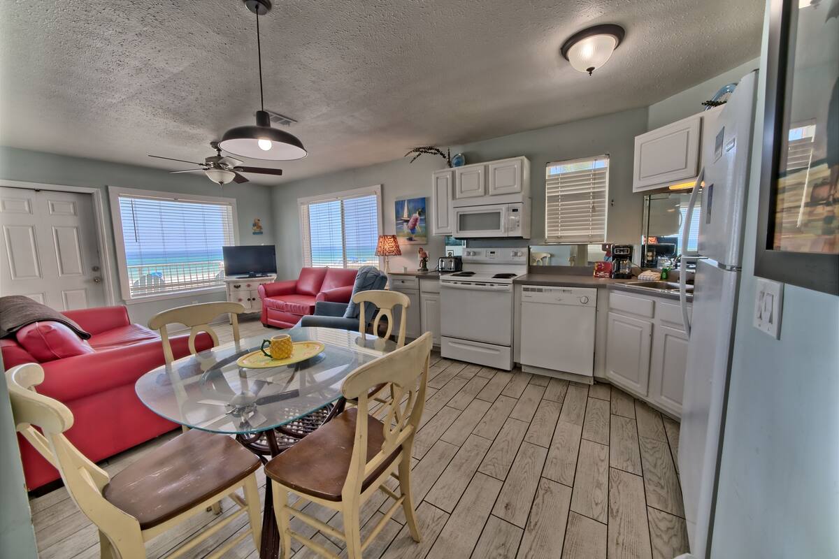 A compact living space with a dining table, red sofa, and kitchen area including a microwave and refrigerator.