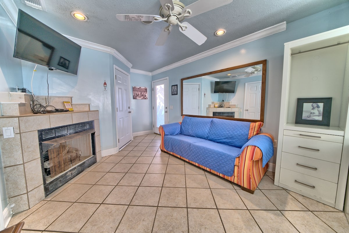 A living room with a fireplace, a sofa, a TV mounted on the wall, and a ceiling fan.