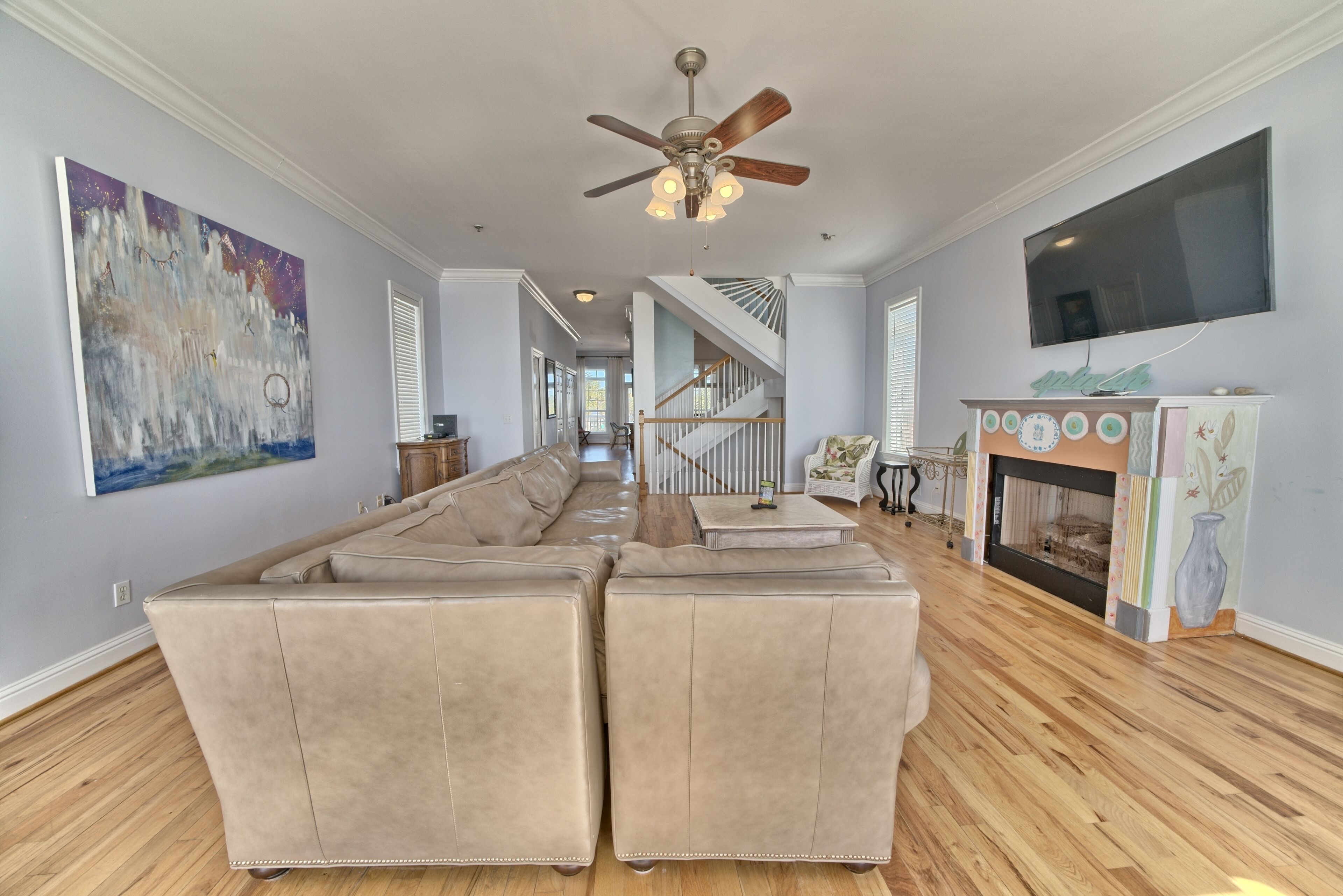 A spacious living room with a large sectional sofa, a ceiling fan, a fireplace, and a TV mounted on the wall.