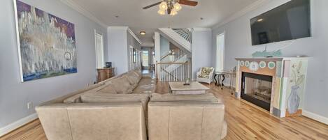 A spacious living room with a large sectional sofa, a ceiling fan, a fireplace, and a TV mounted on the wall.