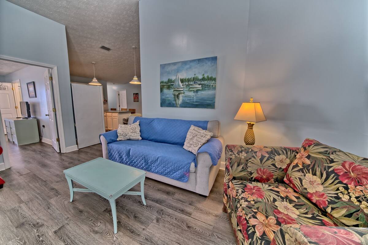 A living room with a blue sofa, a floral sofa, a small table, and a painting of a lake scene.