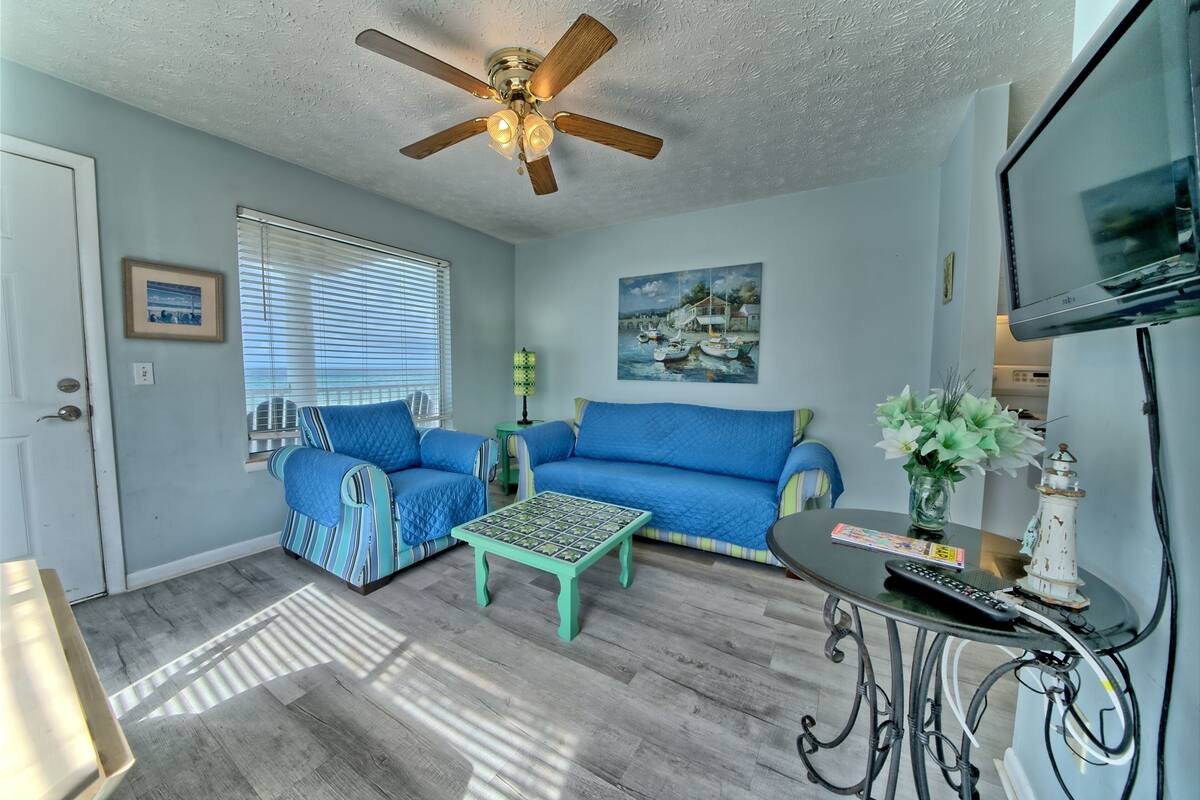 A living room with a ceiling fan, two blue sofas, a coffee table, and a TV on a stand.