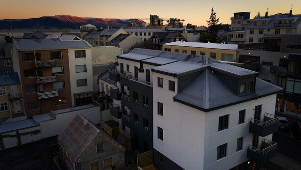 Un edificio residencial de varios pisos con balcones, techo plano y montañas al fondo.
