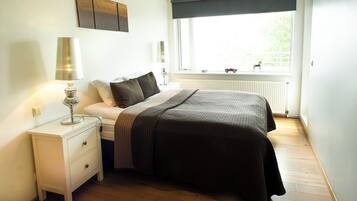 Un dormitorio con cama, mesita de noche, lámpara, ventana con vistas y un radiador.