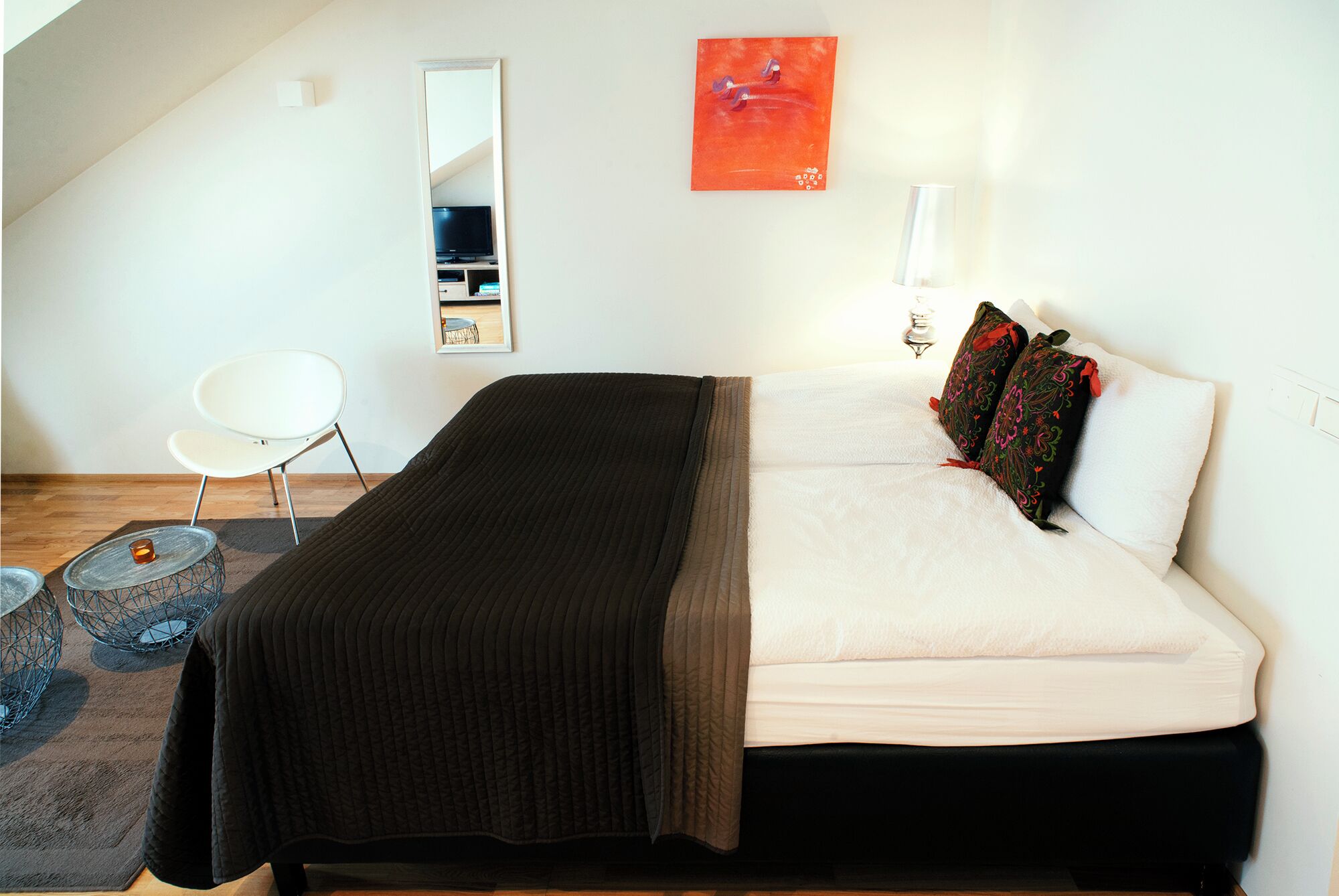 A bedroom with a bed, a chair, a mirror, and a painting on the wall.