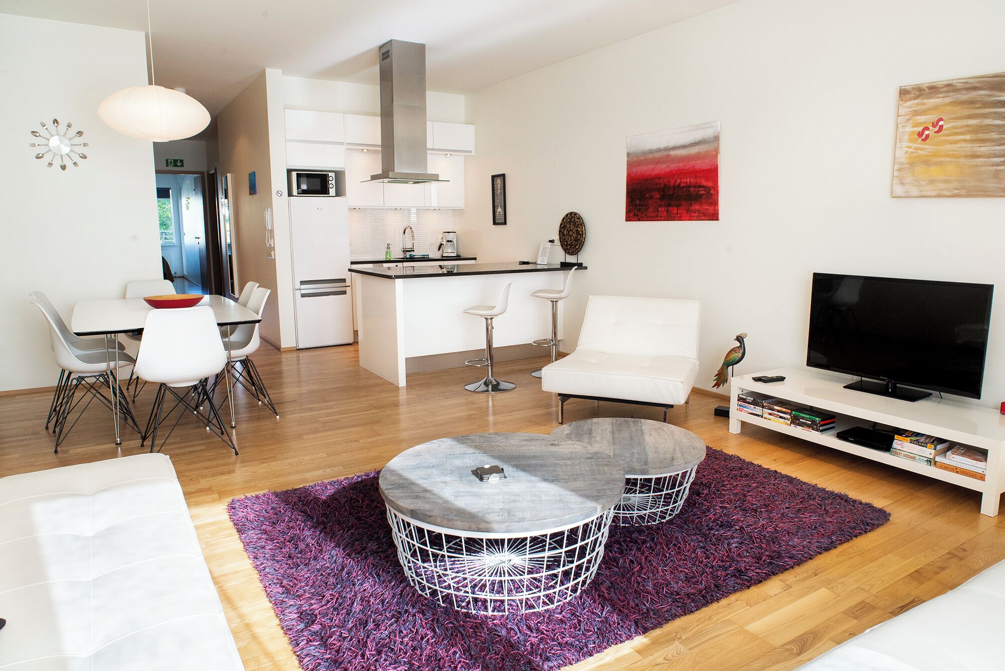A modern living room with a dining area, kitchen, and a flat-screen TV.