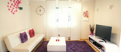 Een moderne woonkamer met een witte bank, een salontafel, een televisie en een groot raam.