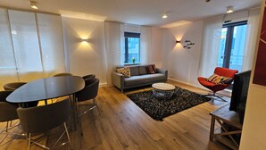 Una sala de estar moderna con un sofá, una mesa de comedor con sillas, una butaca roja, un televisor y una alfombra negra.