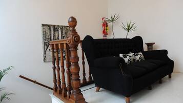 A black sofa with a floral pillow, a wooden staircase, and a fire extinguisher on the wall.