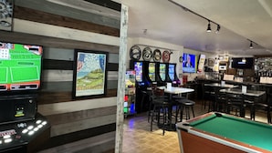 En bar med biljardbord, arkadspel och ett bord för fransk biljard.