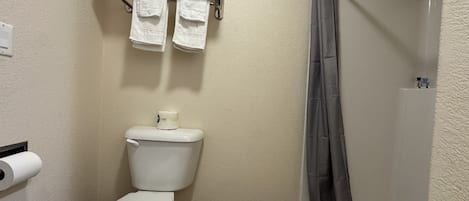A bathroom with a toilet, a towel rack with folded towels, a shower curtain, and a toilet paper holder.