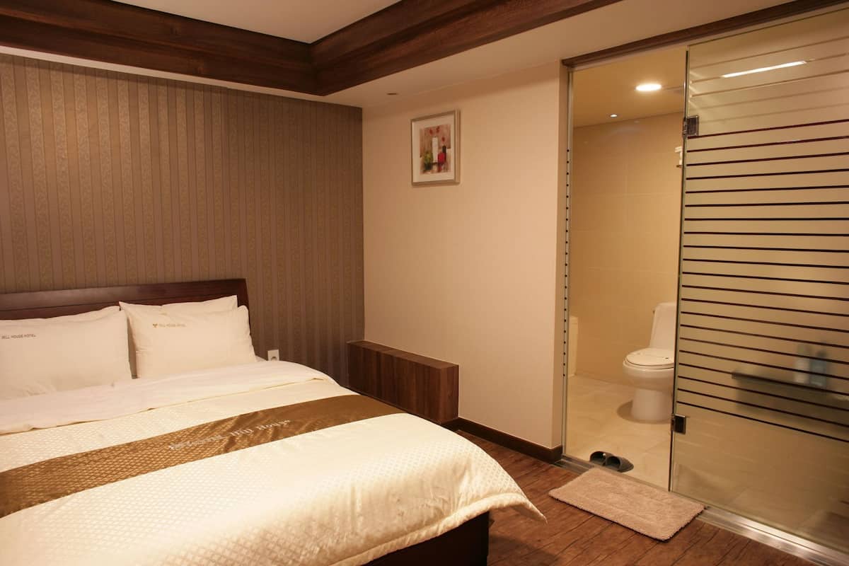 Habitación de hotel con una cama, una mesita de noche, un cuadro enmarcado en la pared y una puerta corrediza de vidrio que da al baño.