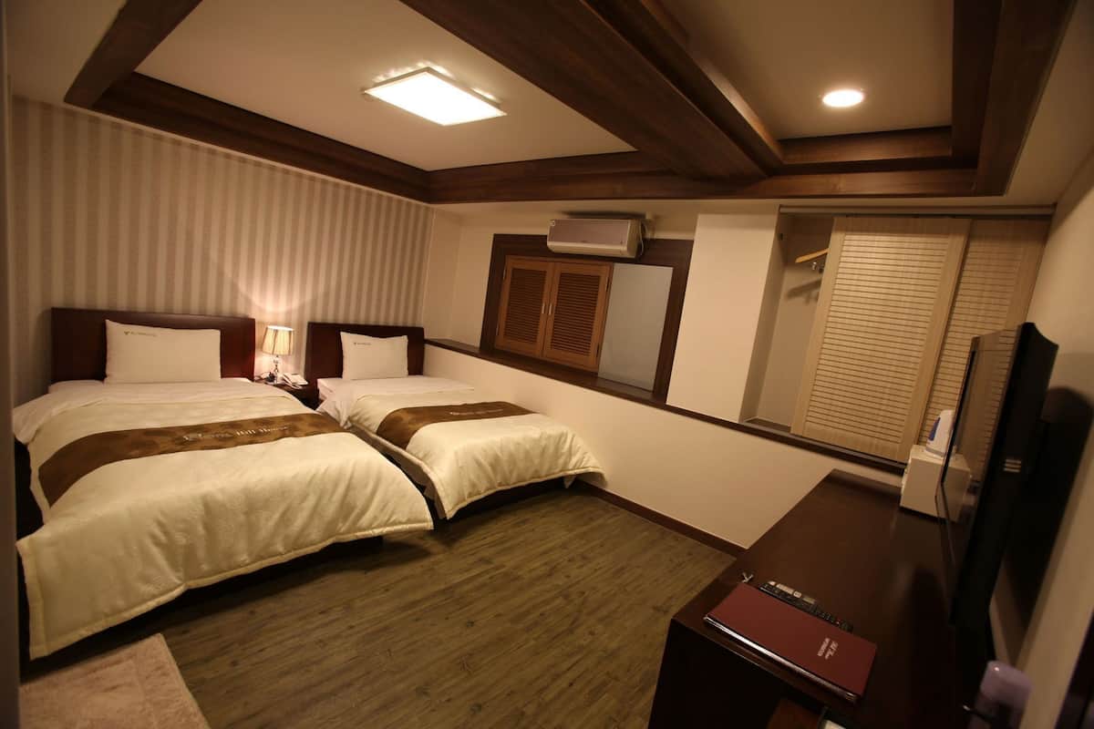 Habitación de hotel con dos camas, un escritorio, un televisor y aire acondicionado.