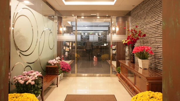 A hotel reception area with a modern design, featuring a reception desk, glass doors, and potted plants. - Hill house Hotel (Seoul)