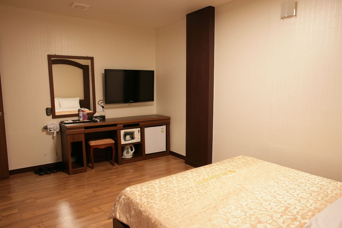 Habitación de hotel con cama, escritorio, silla, televisor, microondas y un refrigerador pequeño.