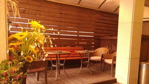 An outdoor seating area with a wooden bench and a round table, surrounded by wicker chairs. - Hill house Hotel (Seoul)