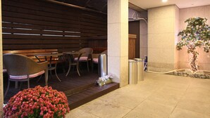 A hotel lobby with a seating area featuring wicker chairs and a wooden bench, a trash bin, and a potted plant with pink flowers. - Hill house Hotel (Seoul)