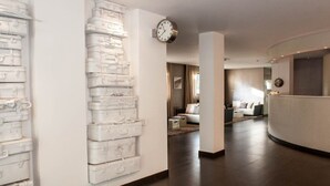 Zona de recepción de hotel con diseño moderno, que incluye un mostrador de recepción, un reloj y una pared con maletas apiladas.