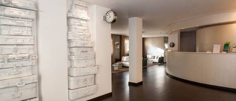 Een receptiehal van een hotel met een modern design, met een receptiebalie, een klok en een muur met gestapelde koffers.