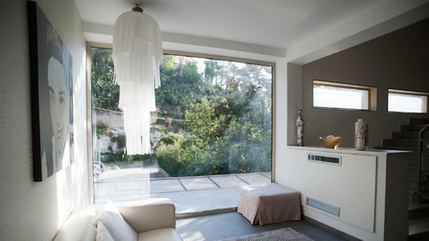 Una sala de estar moderna con un sofá, una mesa de centro de vidrio y vistas a un jardín a través de amplios ventanales.