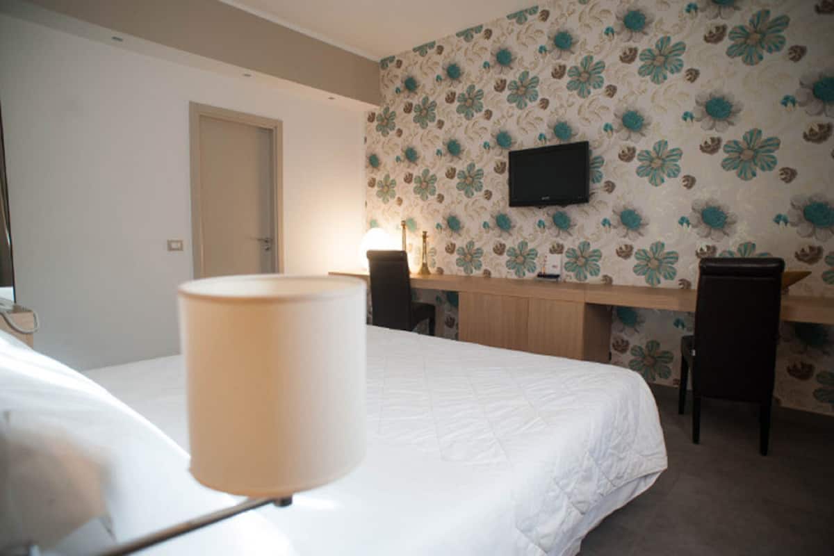 Habitación de hotel con cama, escritorio, dos sillas, televisor y lámpara.