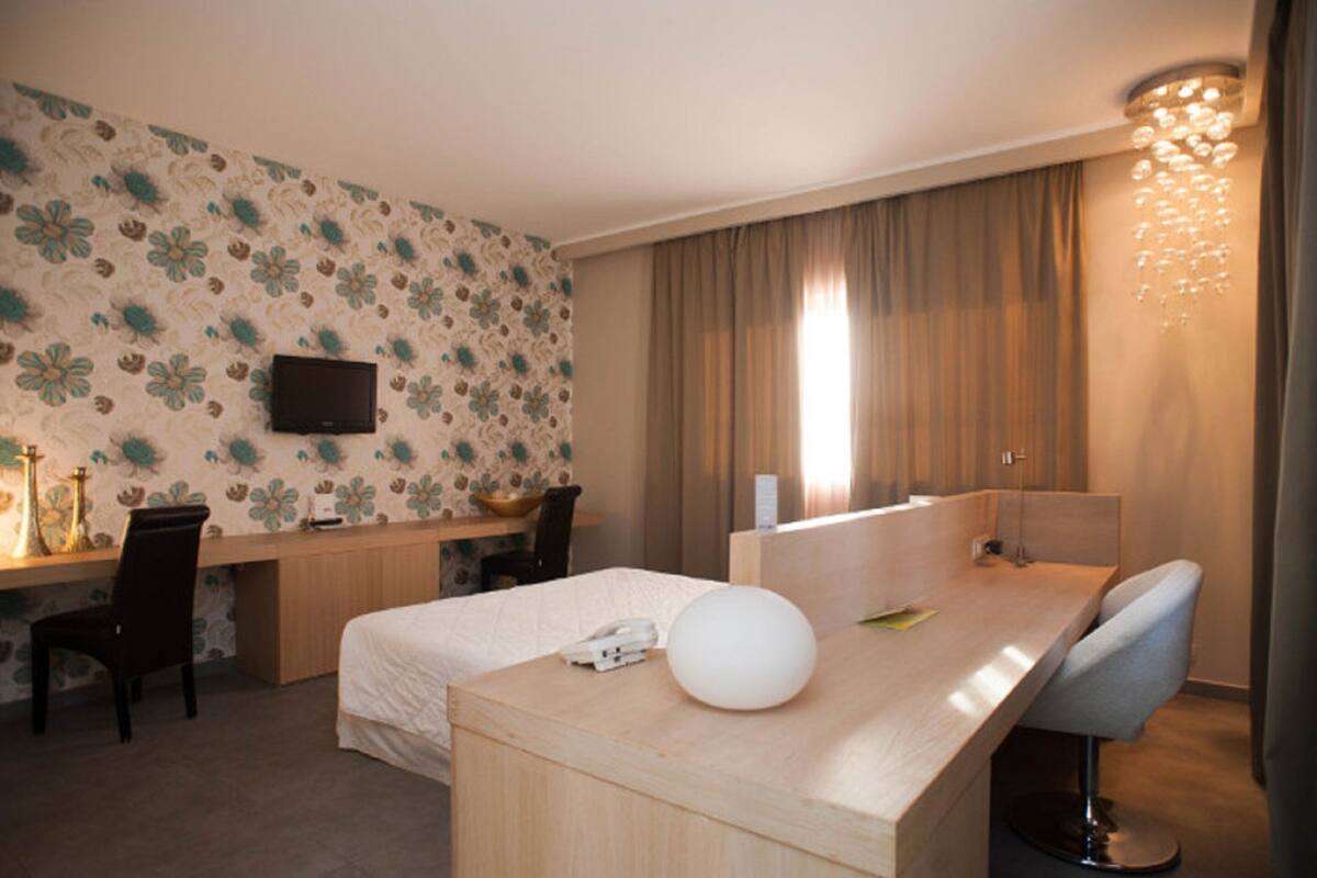 Una habitación de hotel con cama, escritorio, silla y televisión montada en la pared.