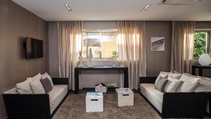 Una sala de estar moderna con dos sofás, una mesa de centro, un televisor montado en la pared y un ventanal con cortinas.