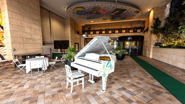 Un piano à queue dans un hall d’entrée, avec un sol carrelé, des chaises blanches et un plafond décoratif.