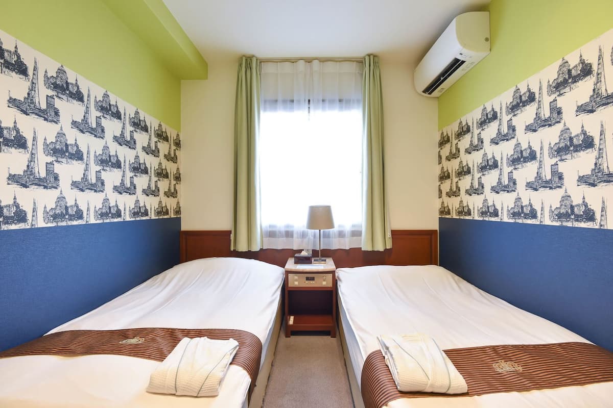 Une chambre d’hôtel avec deux lits, une table de chevet, une lampe et un appareil de climatisation.