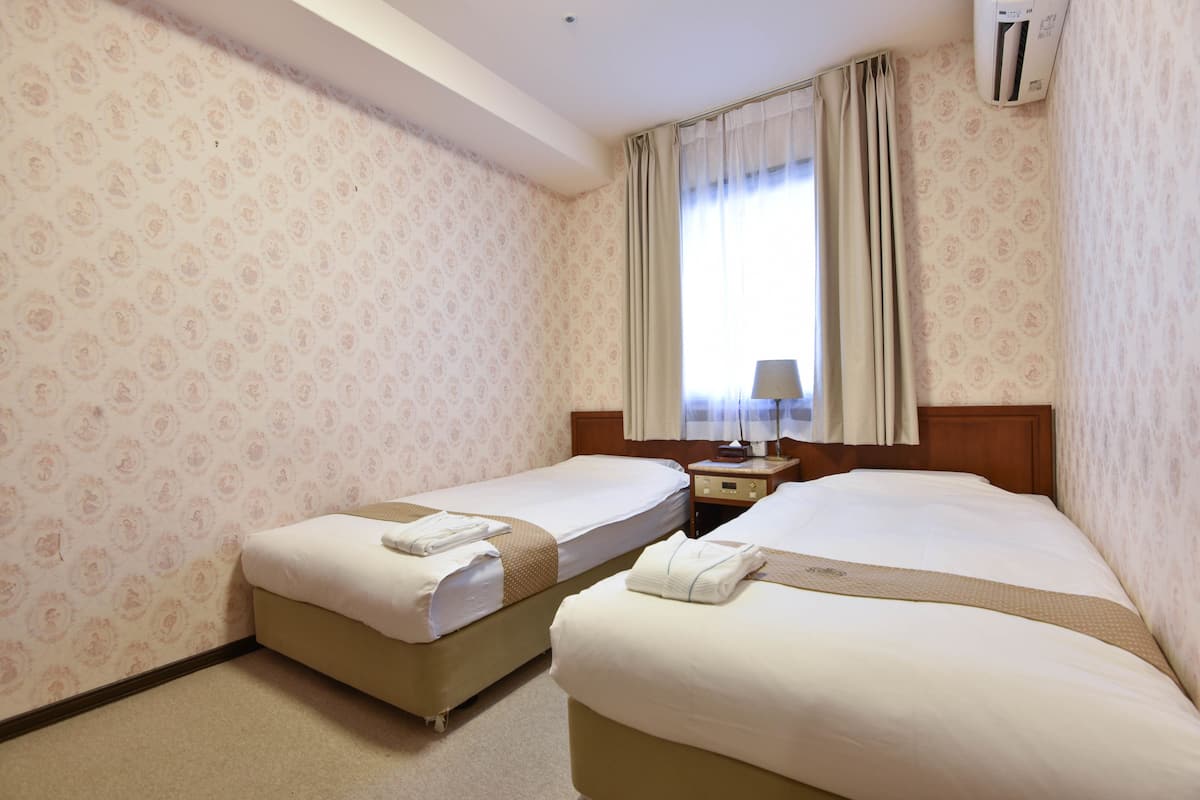 Une chambre d’hôtel avec deux lits, une table de chevet, une lampe et une fenêtre avec des rideaux.