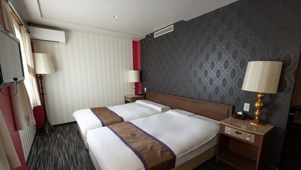 Habitación de hotel con una cama grande, dos mesitas de noche, una lámpara y una ventana con cortinas.